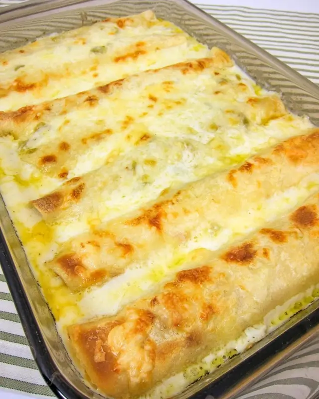 Rolling flour tortilla filled with shredded chicken mixture for white enchiladas