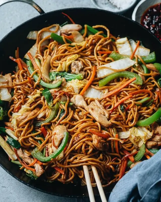 Fresh ingredients for sticky garlic chicken noodles  including chicken breast, garlic cloves, soy sauce,  honey, and noodles laid out on a wooden board