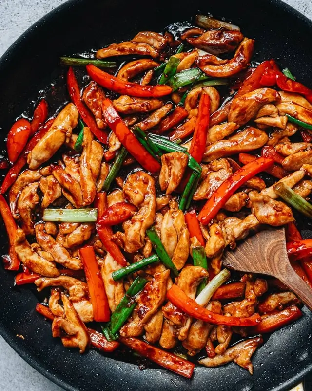 Chicken noodles being tossed in sticky garlic sauce using tongs in a wok over high heat